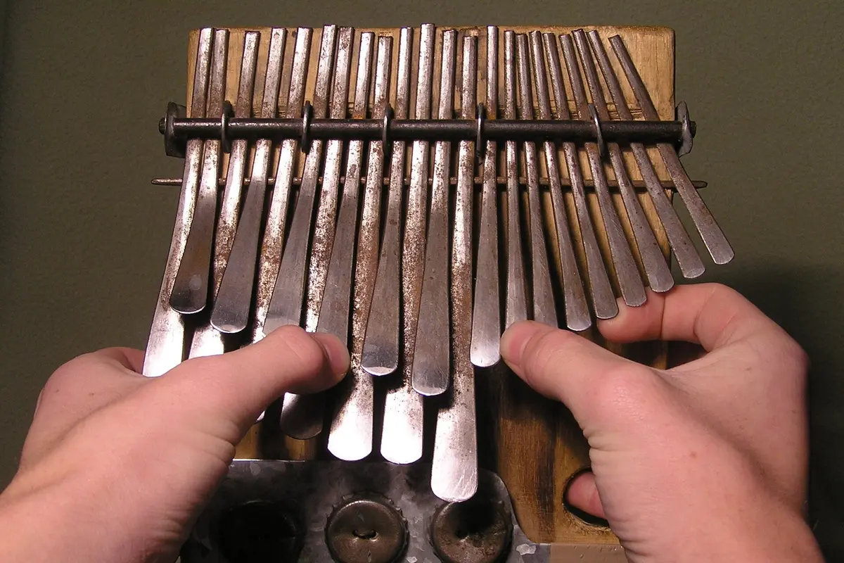 Two hands plucking the steel keys of an mbira dzavadzimu, a board of staggered metal tines fixed to a wooden body